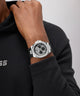 Person wearing a black and silver GUESS Mens Black Silver Tone Analog Watch on a plain background