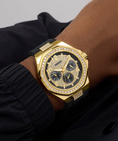 GUESS Mens BLACK GOLD TONE Analog Watch with diamond accents on a person's wrist against a dark background