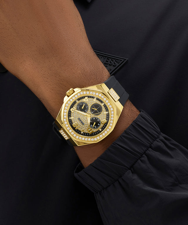 GUESS Mens BLACK GOLD TONE Analog Watch with black face on a person's wrist against a dark background