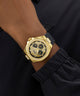 GUESS Mens BLACK GOLD TONE Analog Watch with black face on a person's wrist against a dark background