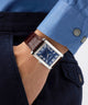 Person wearing a blue shirt with a brown leather strap watch on a white background