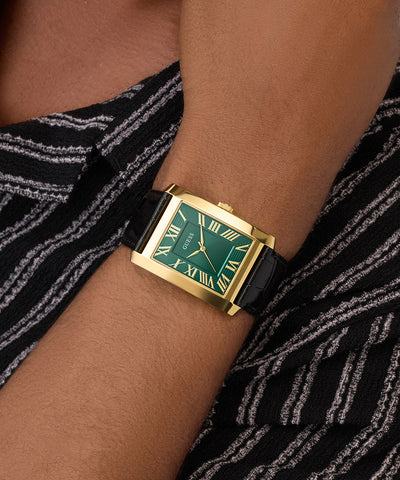 GUESS Mens BLACK GOLD TONE Analog Watch on a wrist with a black and white patterned fabric background