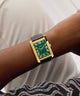 GUESS Mens BLACK GOLD TONE Analog Watch with green face on a wrist against a white background