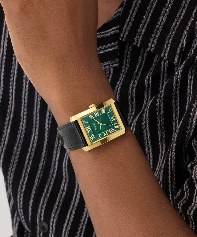 GUESS Mens BLACK GOLD TONE Analog Watch with green face on a wrist against a striped background