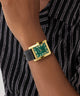 GUESS Mens BLACK GOLD TONE Analog Watch with green face on a wrist against a striped background