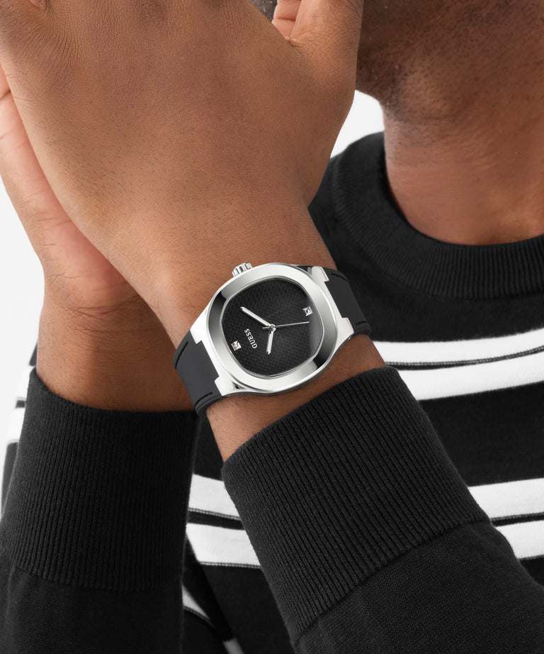 Person wearing a black GUESS Mens Black Silver Tone Analog Watch with a black and white striped shirt