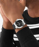 Person wearing a black GUESS Mens Black Silver Tone Analog Watch with a black and white striped shirt