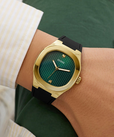 Gold and green GUESS Mens Black Gold Tone Analog Watch on a wrist with a blurred background