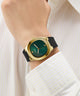 GUESS Mens Black Gold Tone Analog Watch with a green face and black strap on a wrist, against a white background