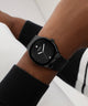 Black GUESS Mens BLACK Analog Watch on a person's wrist with a blurred background