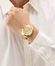 GUESS Mens Gold Tone Analog Watch on a person's wrist with a white shirt background