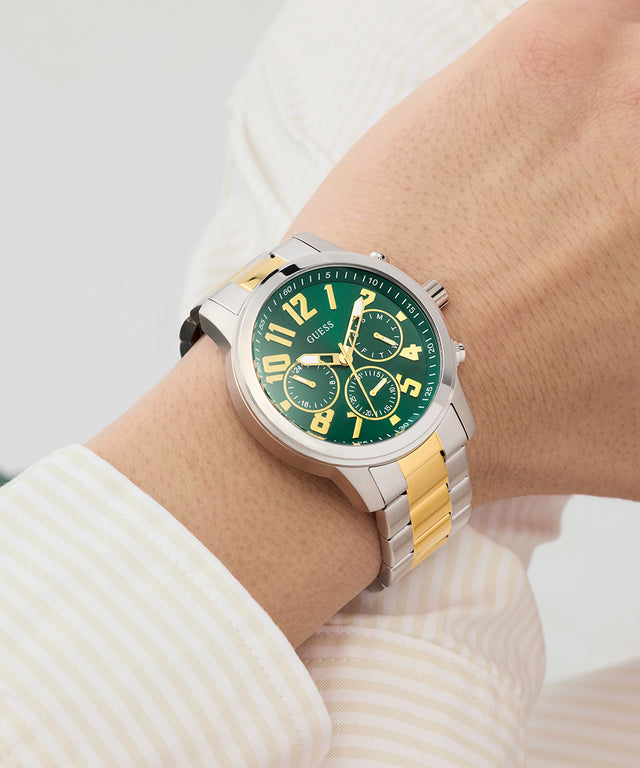 Watch with a green dial and gold accents on a wrist against a light background