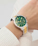Watch with a green dial and gold accents on a wrist against a light background