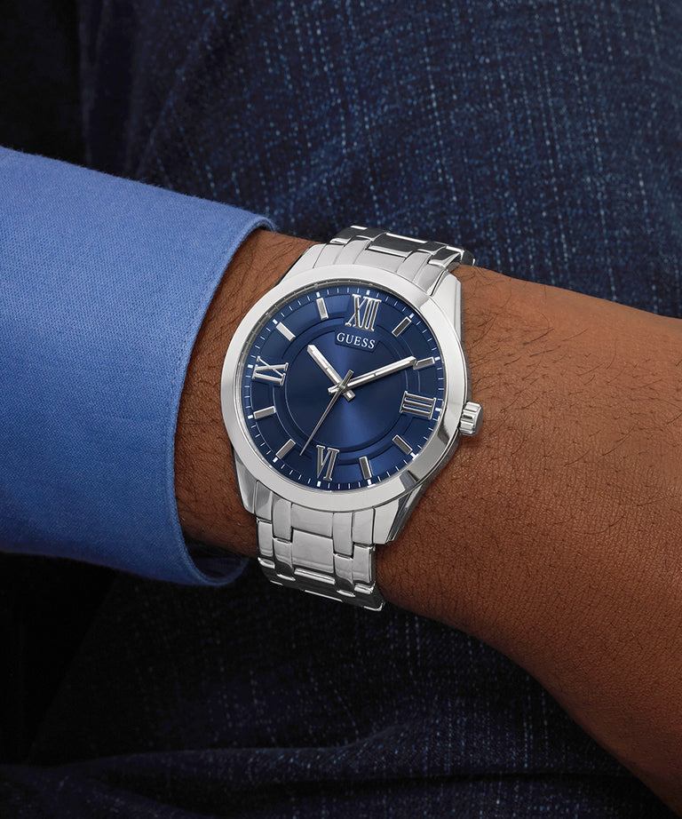 Person wearing a silver GUESS Mens SILVER TONE Analog Watch with a blue face on a wrist, with a blue shirt and dark suit.