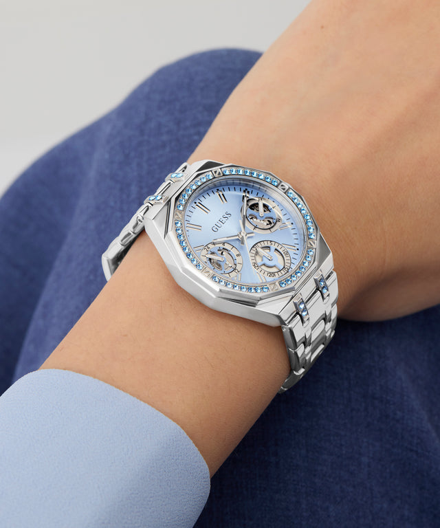 Silver Guess GUESS Ladies Silver Tone Multi-function Watch on a wrist with a light blue background