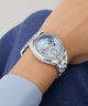 Silver Guess GUESS Ladies Silver Tone Multi-function Watch on a wrist with a light blue background