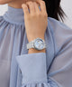 Silver GUESS Ladies Silver Tone Multi-function Watch on a wrist with a light blue dress