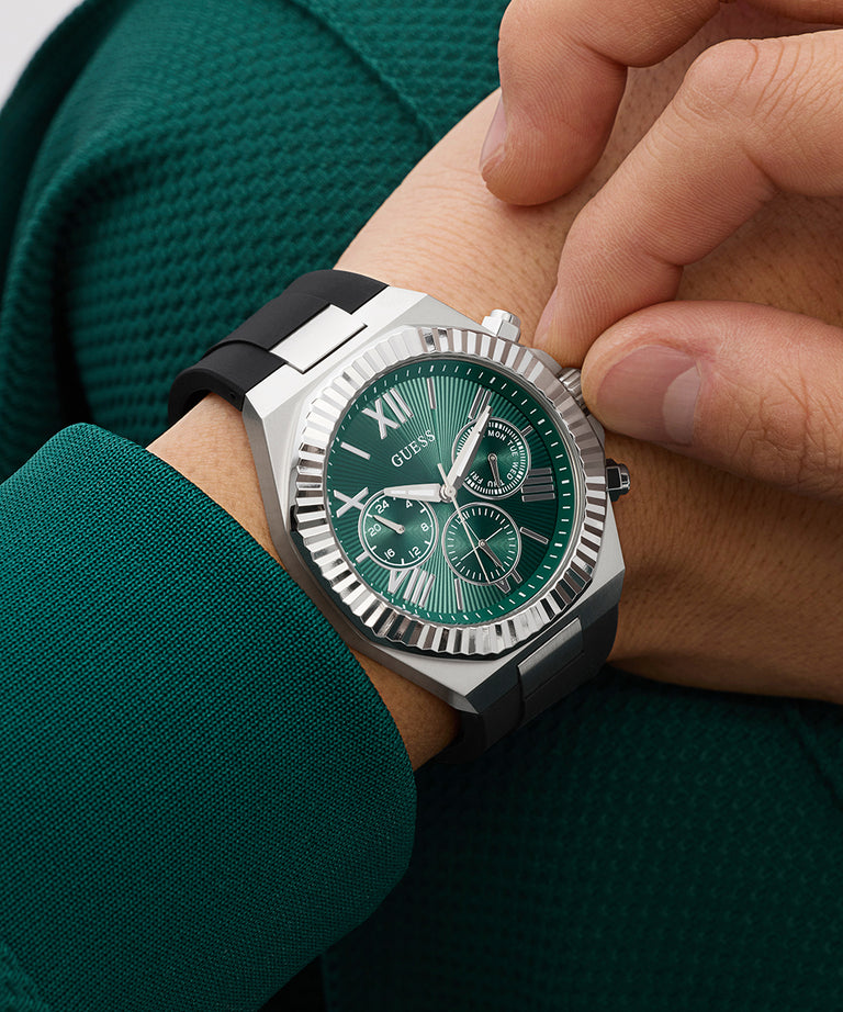 Close-up of a person wearing a green GUESS Mens Equity Black Silver Tone Analog Watch with a detailed face.