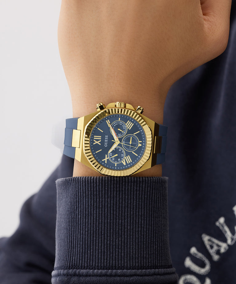 Gold GUESS Mens Equity Blue Gold Tone Analog Watch with blue face on a wrist, wearing a navy sweater.