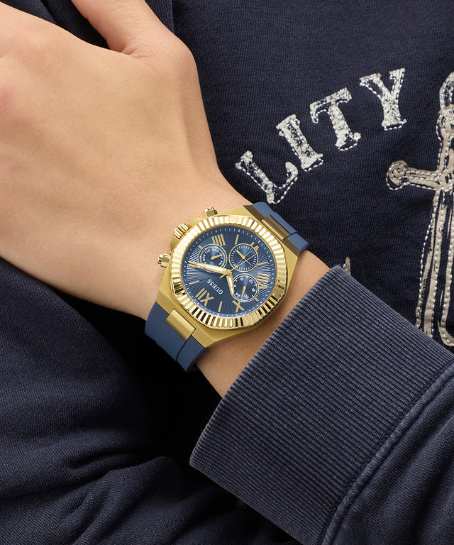 Gold GUESS Mens Equity Blue Gold Tone Analog Watch with blue strap worn on a wrist, against a dark background with text.