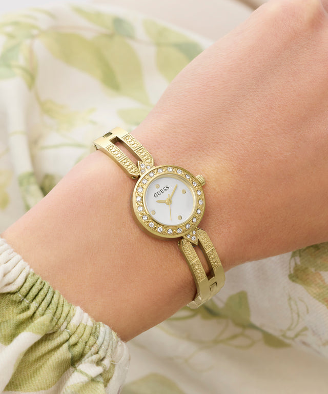 Gold Guess watch on a wrist with a floral background