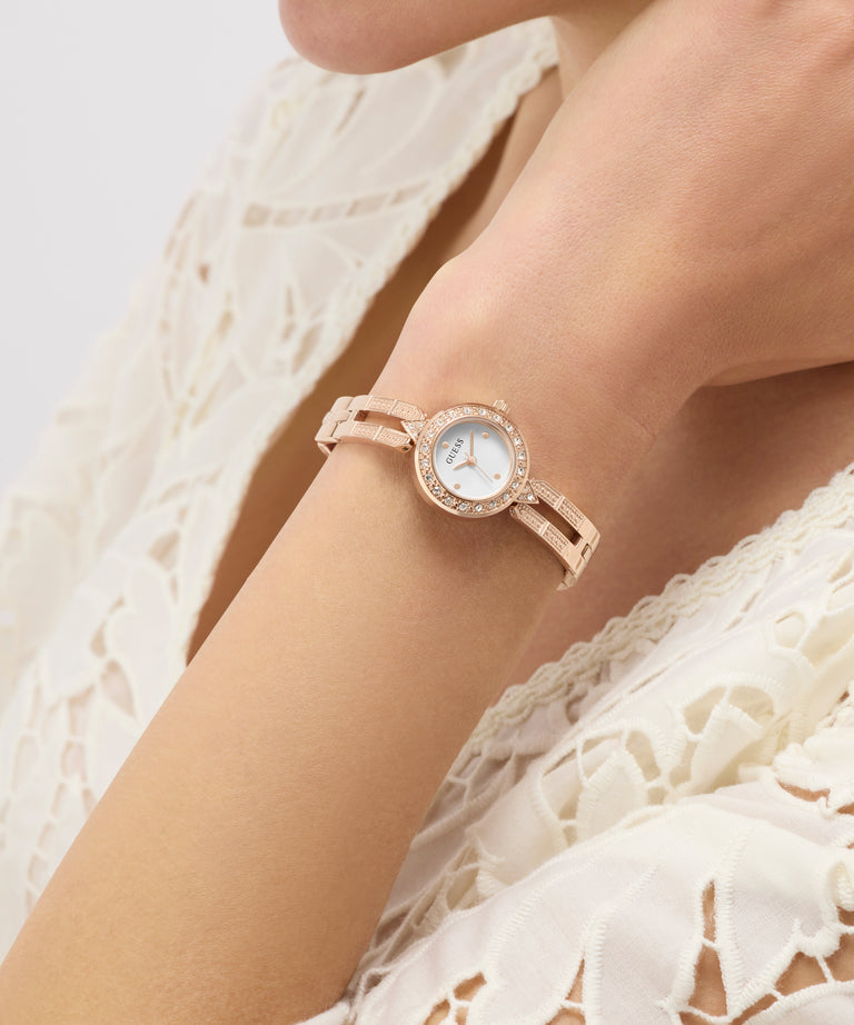 Rose gold GUESS Ladies Rose Gold Tone Analog Watch on a wrist with a white lace garment in the background