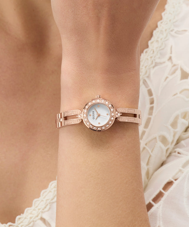 Rose gold GUESS Ladies Rose Gold Tone Analog Watch on a wrist with a blurred background