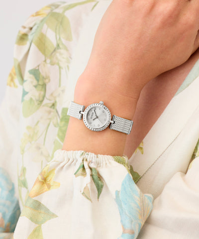 Silver GUESS Ladies Silver Tone Analog Watch on a wrist with a floral-patterned fabric background