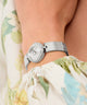 Silver GUESS Ladies Silver Tone Analog Watch on a wrist with a floral-patterned fabric background