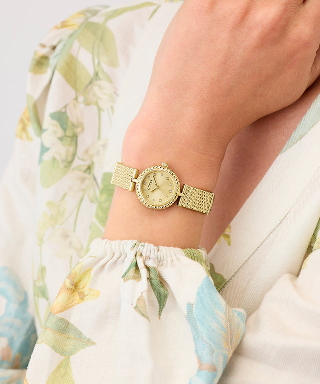 Gold GUESS Ladies Gold Tone Analog Watch on a wrist with a floral-patterned fabric background