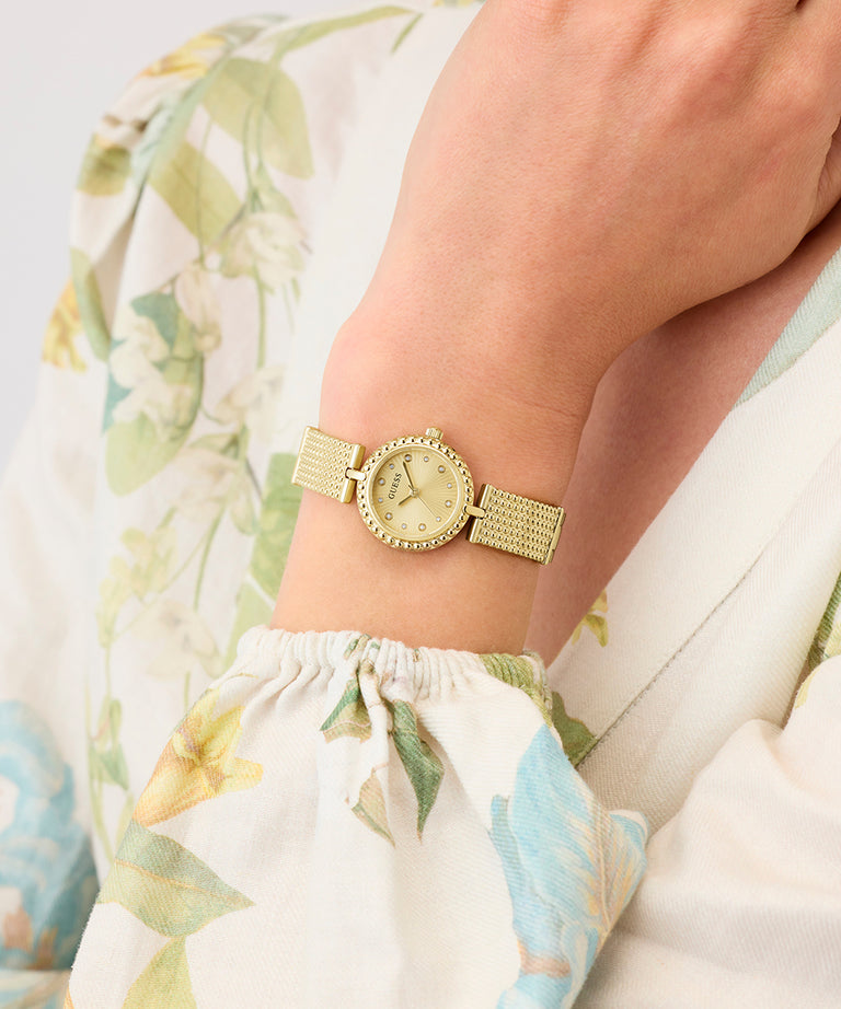 Gold GUESS Ladies Gold Tone Analog Watch on a wrist with a floral-patterned fabric background