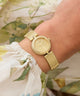 Gold GUESS Ladies Gold Tone Analog Watch on a wrist with a floral background