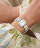 GUESS Ladies Hazel Silver Tone Analog Watch on a wrist with a floral-patterned fabric background