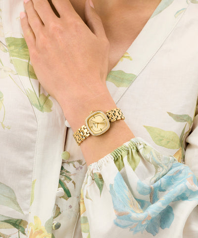 GUESS Ladies Hazel Gold Tone Analog Watch on a wrist with floral-patterned fabric in the background