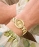 GUESS Ladies Hazel Gold Tone Analog Watch on a wrist with a floral-patterned fabric background
