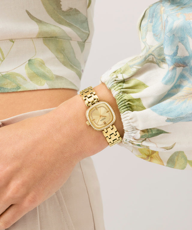 GUESS Ladies Hazel Gold Tone Analog Watch on a wrist with floral-patterned sleeves
