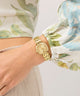 GUESS Ladies Hazel Gold Tone Analog Watch on a wrist with floral-patterned sleeves