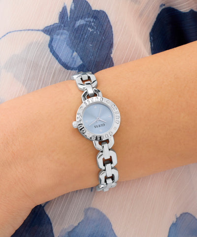 GUESS Ladies Siren Silver Tone Analog Watch on a wrist with a floral-patterned fabric background