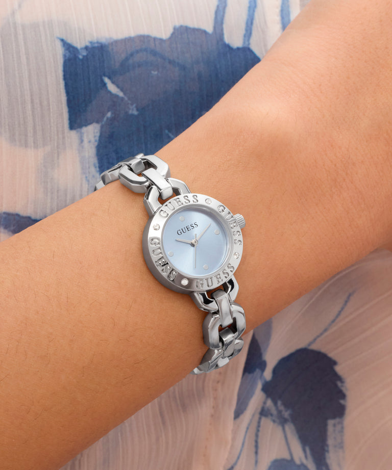 GUESS Ladies Siren Silver Tone Analog Watch on a wrist with a floral-patterned fabric background