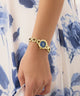 Gold GUESS Ladies Siren Gold Tone Analog Watch with a blue face on a wrist against a floral-patterned background