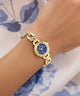 Gold GUESS Ladies Siren Gold Tone Analog Watch with a blue face on a wrist against a floral background