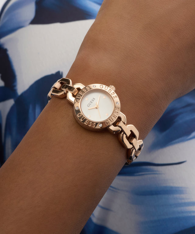 GUESS Ladies Siren Rose Gold Tone Analog Watch on a wrist with a blue and white patterned background