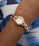 GUESS Ladies Siren Rose Gold Tone Analog Watch on a wrist with a blue and white patterned background