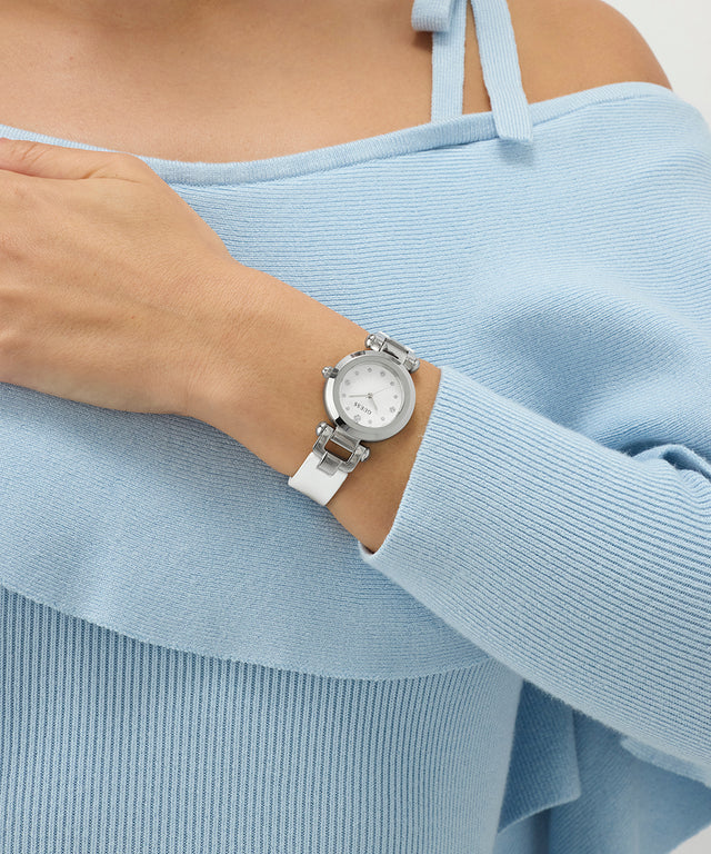 Person wearing a silver watch with a white strap on a light blue sweater.