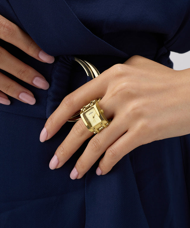 GUESS Ladies Mod Heavy Metal Gold Tone Analog Watch Ring with a small clock face on a hand wearing a navy blue garment.