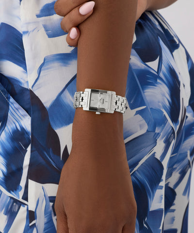 Silver GUESS Ladies Silver Tone Analog Watch on a wrist with a blue and white patterned fabric background