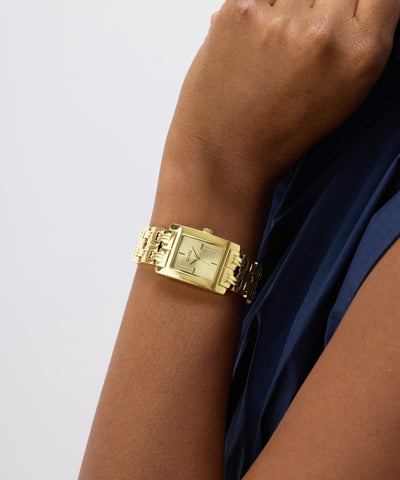 Gold GUESS Ladies Gold Tone Analog Watch on a wrist with a plain background