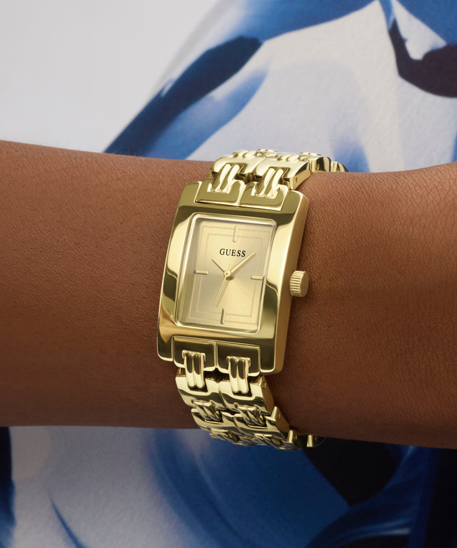 Gold GUESS Ladies Gold Tone Analog Watch on a wrist with a blue and white patterned background