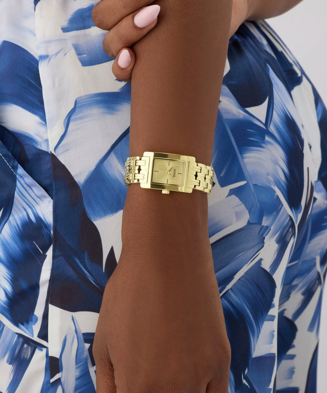 Gold GUESS Ladies Gold Tone Analog Watch on a wrist with a blue and white patterned background