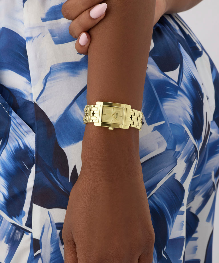 Gold GUESS Ladies Gold Tone Analog Watch on a wrist with a blue and white patterned background